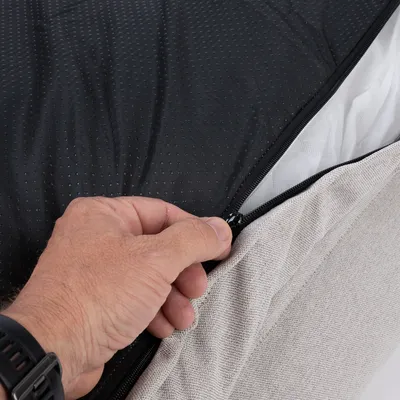 Close-up of a hand opening a zip on black and beige fabric. Shows removable cover of a product.