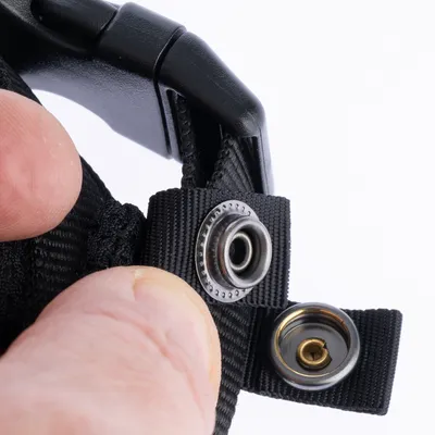Close-up van een zwarte riem met metalen drukknoopsluiting, vastgehouden door een hand.