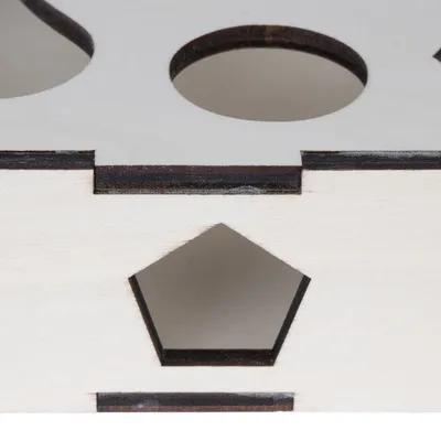 Détail d’un objet en bois clair avec découpes géométriques, dont un cercle et un pentagone visibles sur la surface et le côté.