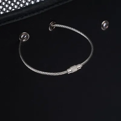 Close-up van een zilveren staalkabel met sluiting, bevestigd aan een zwart oppervlak met metalen ogen.