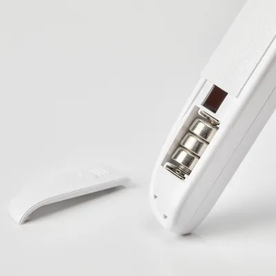 Nahaufnahme eines weissen Geräts mit geöffnetem Batteriefach, drei sichtbaren Batterien und abgenommener Abdeckung.