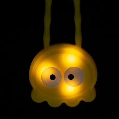Gelbes LED-Spielzeug in Form eines leuchtenden Gesichts mit grossen Augen, geeignet für dunkle Umgebungen.