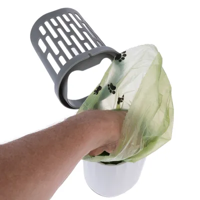 Una mano coloca una bolsa verde con estampado de huellas en un cubo de basura blanco con tapa gris.