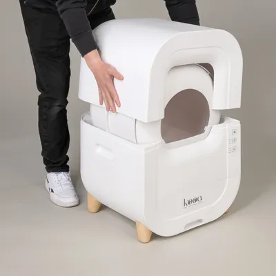 kooa cat litter box with removable lid, white, on wooden legs. Person demonstrates easy assembly by lifting the top part.