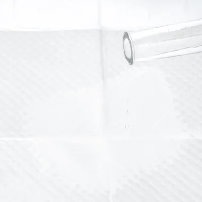 Tube en verre versant de l’eau sur une surface blanche absorbante à motif quadrillé, montrant la capacité d’absorption du matériau.