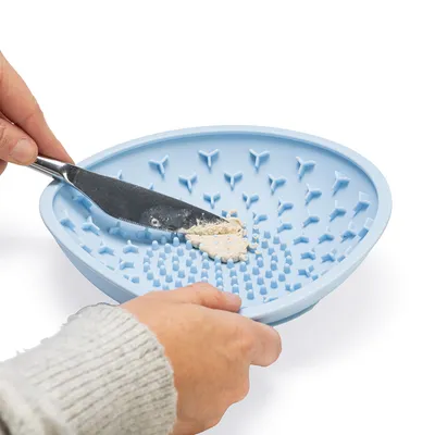 Hand trägt mit Messer Futter auf eine blaue Silikon-Futtermatte mit Noppen auf.