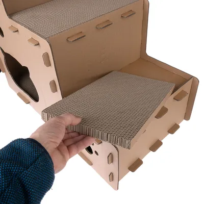 Kartonhaus mit herausnehmbarer Wellpappe-Einlage, handgehalten. Zeigt austauschbare Kratzfläche.