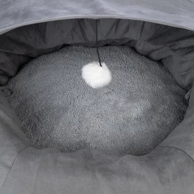 Grey, round pet bed with soft plush interior and hanging white play ball on a string.