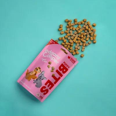 Edgard Cooper Puppy Bites eend, roze verpakking met kleine ronde snacks zichtbaar. Tekst: 'small in size', 'DUCK', 'PUPPY BITES'. Illustratie van puppy en kat op de zak.
