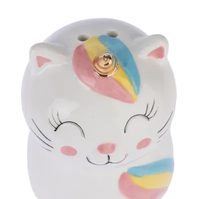 Figurine en céramique blanche en forme de chat avec corne dorée, motifs colorés rose, jaune et bleu sur la tête et la patte, trois trous visibles sur le dessus.