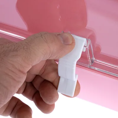Hand zeigt, wie ein weisser Verschluss an einer rosa Box geöffnet wird.