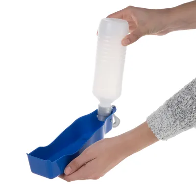 Hand hält eine blaue tragbare Trinkflasche mit integriertem Napf, Wasser wird aus der Flasche in den Napf gegossen.