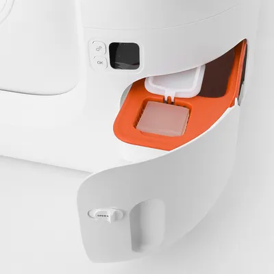 Compartiment ouvert d’un appareil blanc avec plateau orange, bouton « OK » et indicateur, contenant un bloc solide dans une grille. Levier marqué « OPEN ».