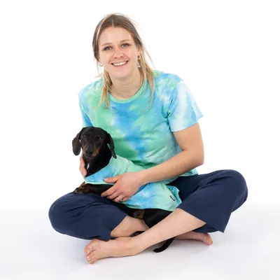 Cane con un cappotto per cani turchese, tenuto da una persona con una maglietta turchese-verde abbinata. Il prodotto mostra abbigliamento per cani.