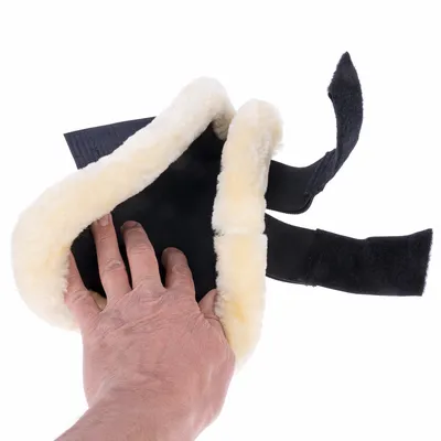 Main insérant une patte dans une protection noire bordée de fausse fourrure beige avec deux sangles à scratch visibles, matériau textile et imitation fourrure clairement apparents.