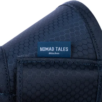 Étiquette sur tissu bleu foncé avec motif hexagonal, texte visible : NOMAD TALES München