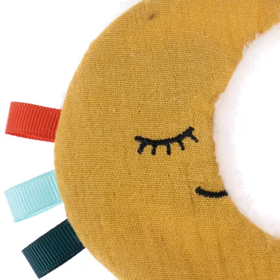 Crescent-shaped fabric toy in yellow with embroidered face and coloured ribbons: red, turquoise, dark green. Made of fabric and plush.