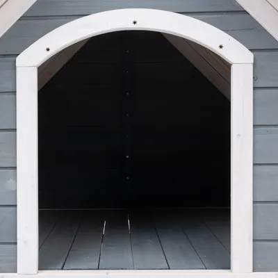 Casota de madeira cinzenta para cães com moldura branca e entrada aberta, interior visível.