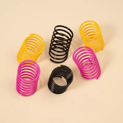 Seks spiralformede legetøj i gul, sort og pink af plast på beige baggrund.