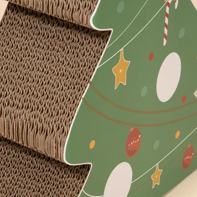 Kratzbrett aus Wellpappe in Form eines Weihnachtsbaums mit grüner Oberfläche und bunten Ornamenten.