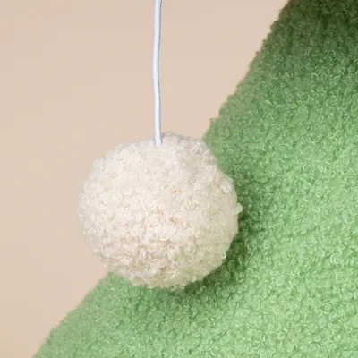Zawieszona zabawka z białego, puszystego materiału na sznurku na zielonym tle.