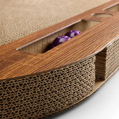 Cat toy made of corrugated cardboard with wooden surface and integrated compartment containing two purple balls.
