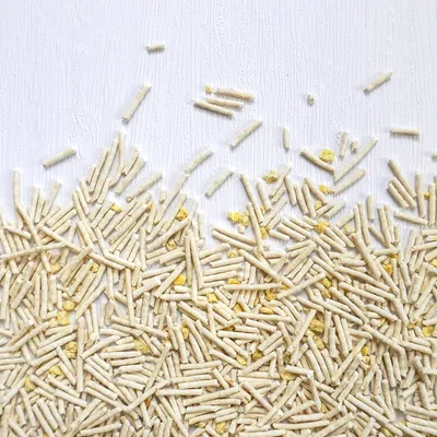 Close-up of dry food pellets and yellow flakes scattered on a white surface, showing product texture and shape.