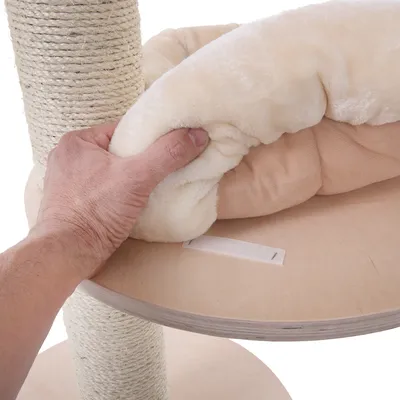 Hand showing soft, cream-coloured cushion on a wooden platform next to a scratching post wrapped in sisal.