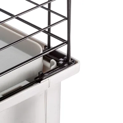 Coin d’une cage pour animaux en plastique blanc avec grille métallique noire, bac intérieur amovible visible.