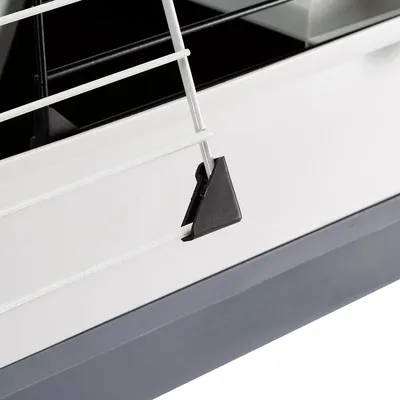 Détail de la grille métallique blanche avec attache en plastique noir sur le rebord d’une cage pour petits animaux, fond gris clair et bac inférieur visible.
