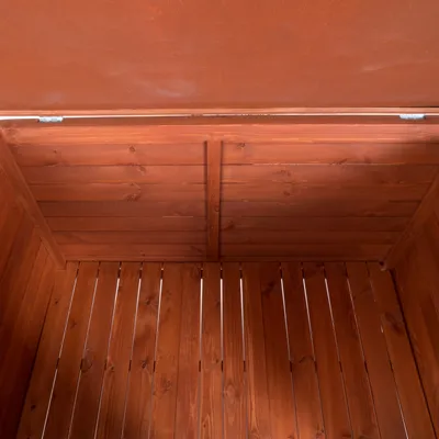 Vista interior de una caseta de madera con techo abatible y paredes de listones, mostrando el material y acabado del interior. Vista interior de una caseta de madera con techo abatible y paredes de listones, mostrando el material y acabado del interior.