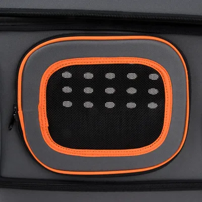 Détail d’une fenêtre en maille noire avec bordure orange sur un sac ou une caisse de transport gris, fermeture éclair visible à gauche.