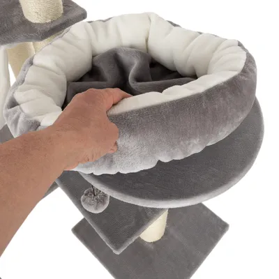 Hand zeigt abnehmbares, gepolstertes Kuschelbett in Grau und Weiss auf einem Kratzbaum mit Sisalstämmen.