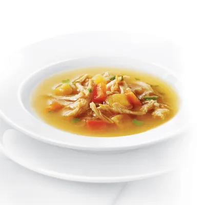 Primer plano de un cuenco con sopa clara que contiene trozos de pollo, zanahorias y hierbas.