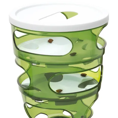 Groene kunststof voerpuzzel met drie lagen, witte schijven en openingen; brokjes zichtbaar op verschillende niveaus.