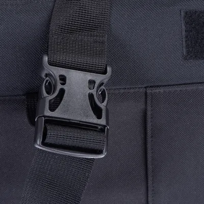 Gros plan sur une boucle en plastique noir avec sangle textile noire, fixée sur un tissu noir épais. Aucun texte ou marque visible.
