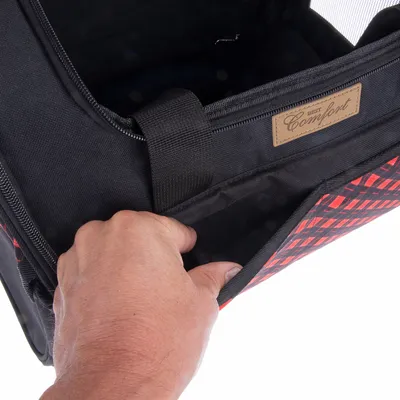 Sac de transport noir et rouge avec étiquette « Best Comfort », main ouvrant une poche extérieure à fermeture éclair, tissu visible.