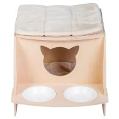 Cuccia in legno chiaro con ingresso a forma di testa di gatto, cuscino superiore beige e due ciotole bianche integrate alla base.