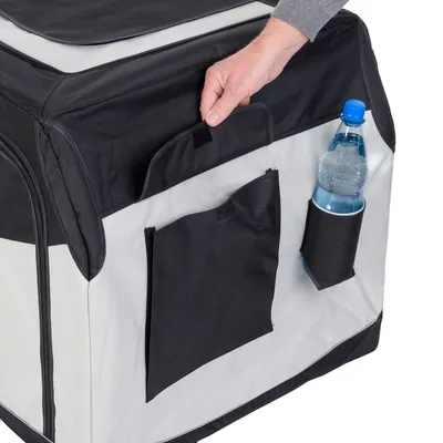 Draagbare stoffen transportbox met zwarte vakken, een hand die het bovenste vak opent en een fles water in een zijvak. Zichtbare ritsen aan de zijkant.