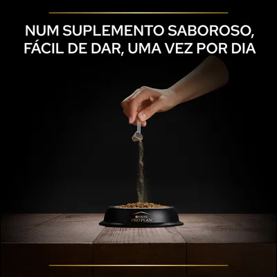 Mão a deitar suplemento em pó sobre ração numa taça preta com o texto: Num suplemento saboroso, fácil de dar, uma vez por dia. Marca visível: Purina Pro Plan.