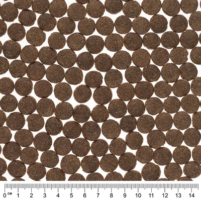 Okrogli peleti suhe hrane, razporejeni v mreži. Spodaj je merilo v centimetrih od 0 do 14 za prikaz velikosti posameznega peleta.