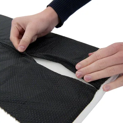 Nahaufnahme von Händen, die eine schwarze rutschfeste Unterlage mit gepunkteter Textur auf weissem Stoff anpassen.
