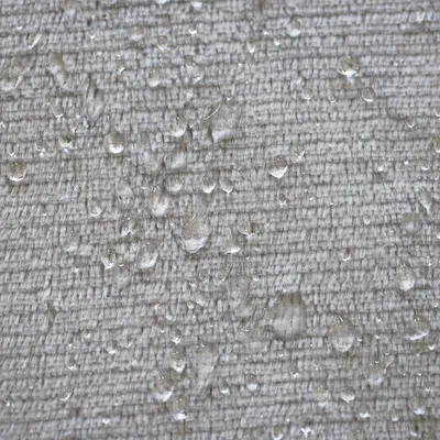 Gros plan sur tissu beige avec gouttes d’eau visibles à la surface. Le matériau et la couleur sont clairement observables.