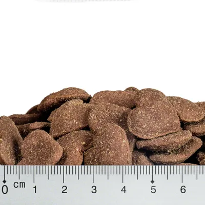 Detailný záber na hnedé granule v tvare srdca s pravítkom na určenie veľkosti, viditeľná stupnica v centimetroch.