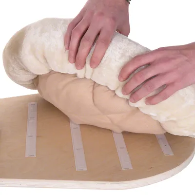 Händer som fäster en beige plyschbädd med kardborreband på en träskiva. Fyra synliga kardborreband på skivan.