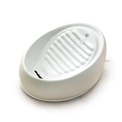 Fuente de agua blanca para mascotas con superficie acanalada y chorro de agua visible, fabricada en material cerámico.