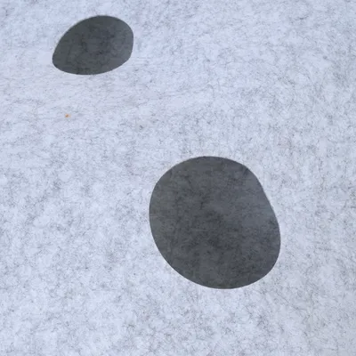 Graue Filzoberfläche mit zwei ovalen, dunklen Ausschnitten. Materialstruktur sichtbar.