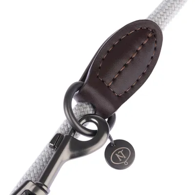 Close-up of a grey dog lead with brown leather trim, metal carabiner, and round tag engraved with logo 'N'.