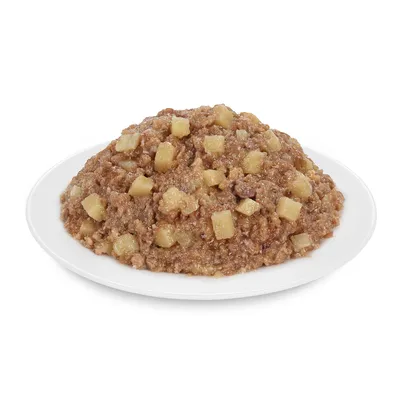 Barna színű, darabos állagú nedves állateledel fehér tányéron, látható sárgás kockákkal keverve.