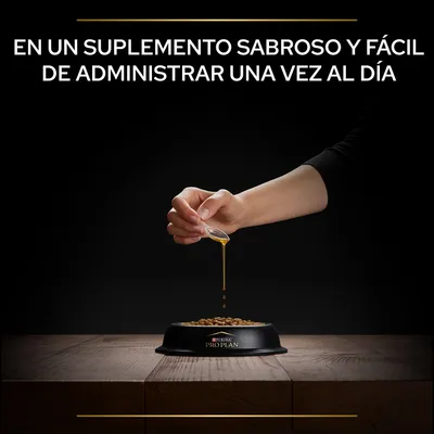 Texto: En un suplemento sabroso y fácil de administrar una vez al día. Mano vertiendo líquido sobre croquetas en cuenco negro con la marca Purina Pro Plan visible.
